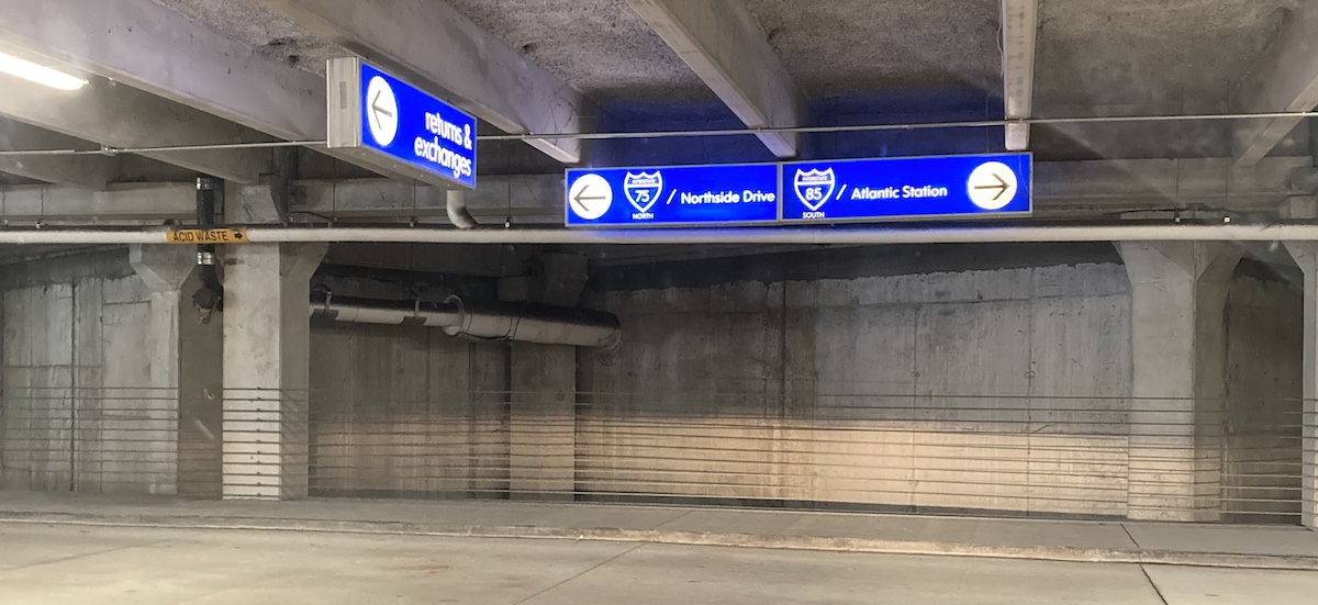 inside of a parkign garage with blue signs hanging from the ceiling one pointing left to interstate north the other pointing right to interstate south